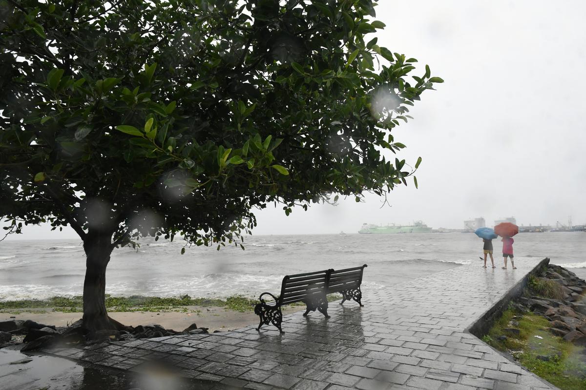 Tourists carry umbrellas to watch the rough sea during heavy rains at Fort Kochi on Thursday. 