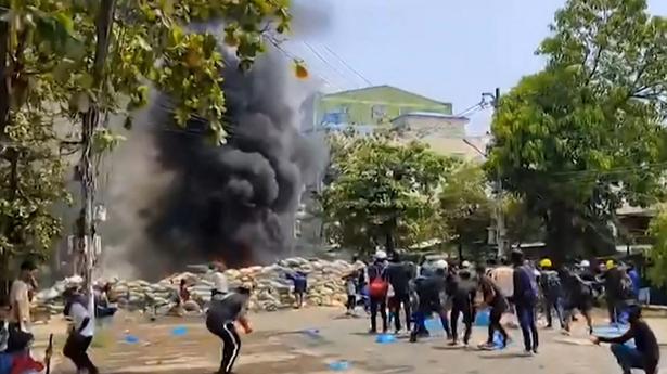 This screengrab from a UGC video provided to AFPTV from an anonymous source and taken on March 27, 2021 shows protesters watching as smoke rises from a burning makeshift barricade during a demonstration against the military coup in Yangon's Thaketa township. 